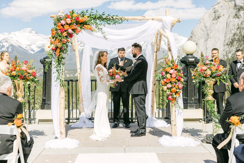 A beautiful wedding ceremony on the terrace at Banff Springs Hotel, featuring the bride and groom exchanging vows with stunning mountain views in the background.