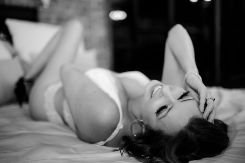 black and white little rock bridal boudoir photos of woman on a bed with her hand in her hair as she wears a white underwear set