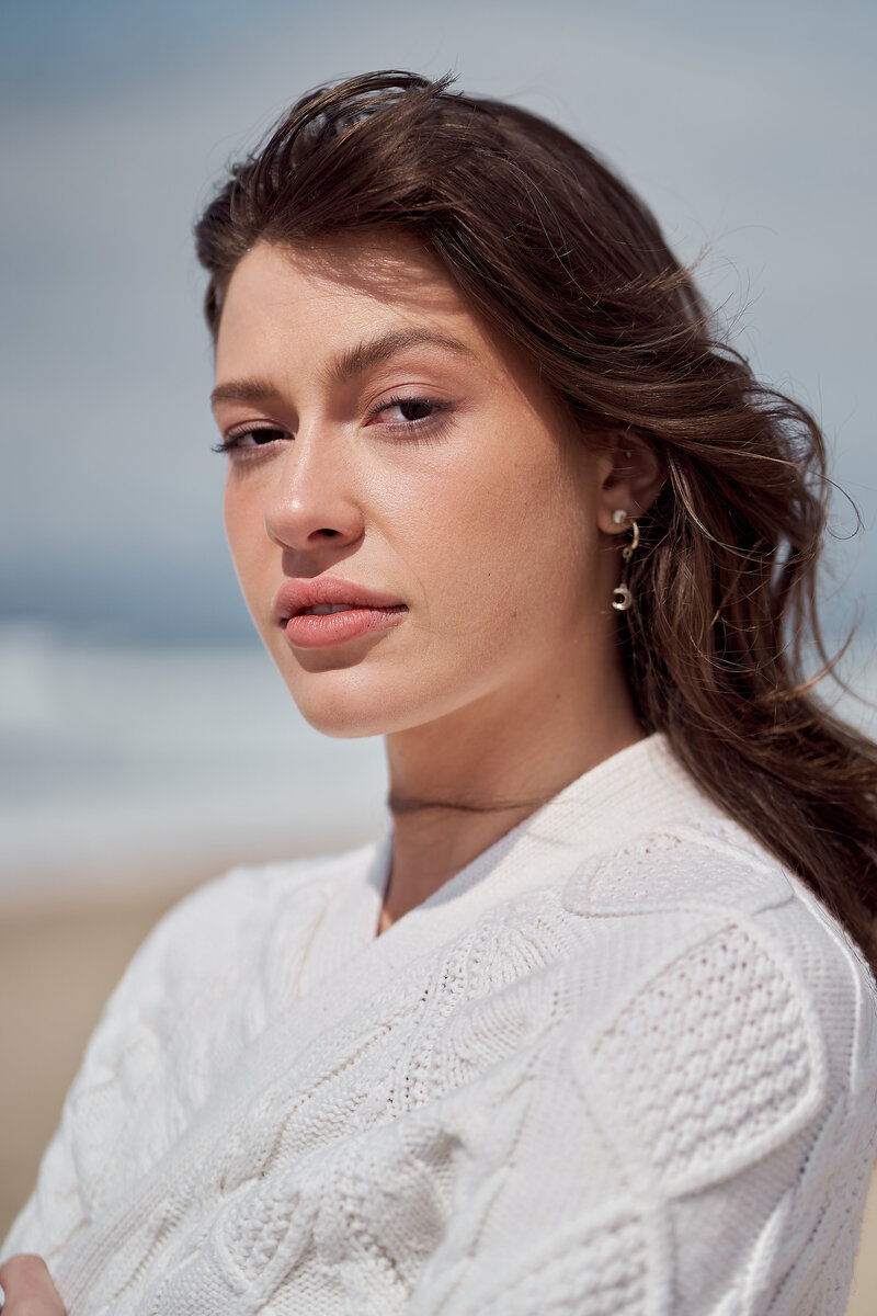 Close up of a young woman with brown hair blowing in the wind wearing a knit white sweater