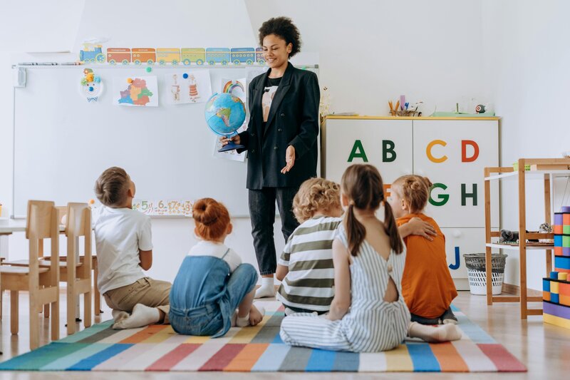 teacher holding globe with students sitting on floor in front of her