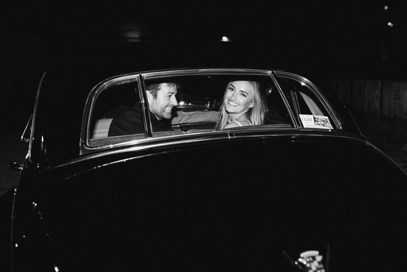 black and white photo of bride and groom in classic getaway car
