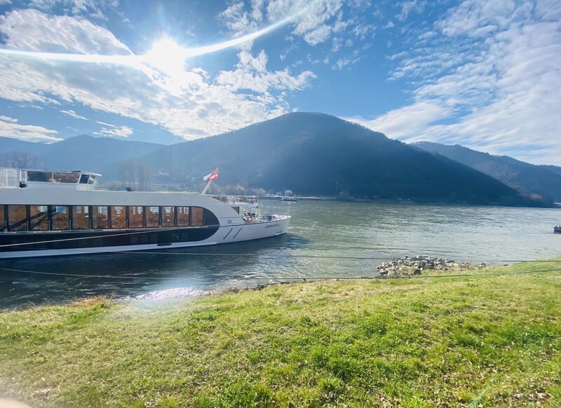 AmaWaterways river cruise ship docked on the Danube river with lush green hills in the background