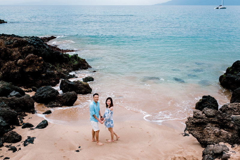 Couple photography at Maluaka Beach with clear, cool blue water and rocks around them.