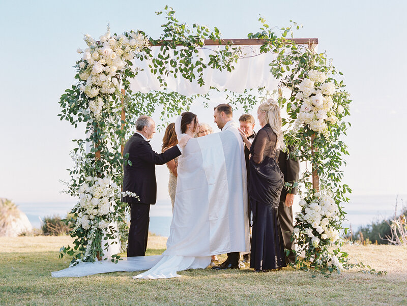 couple during wedding ceremony standing under hoopah decorated with white flowers in santa barbra