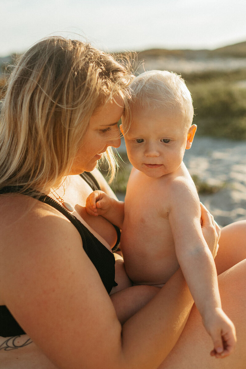 Molly, a San Diego photographer, holding her baby while sitting at the beach, sharing a quiet moment together