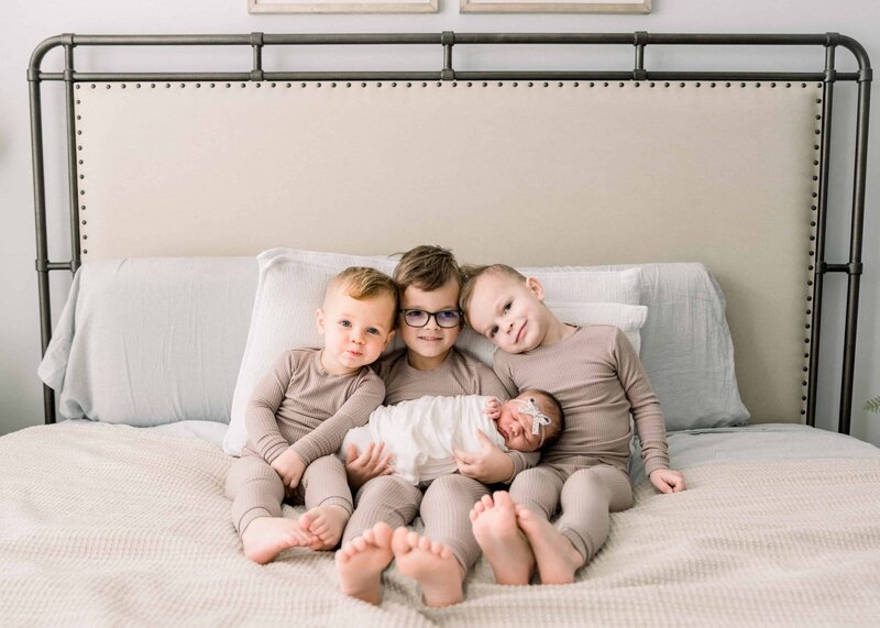 3 little boys hold their new baby sister