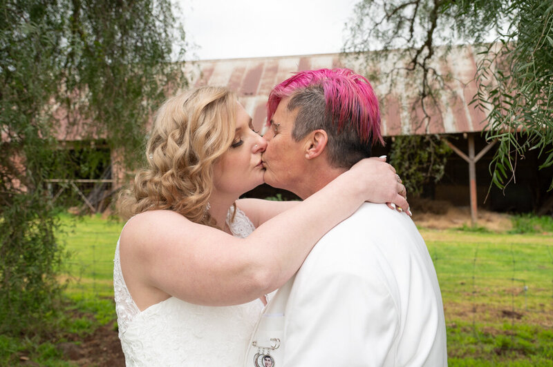 Rustic scenery with a  wedding couple kissing in front of a rustic barn. White and pink theme.
