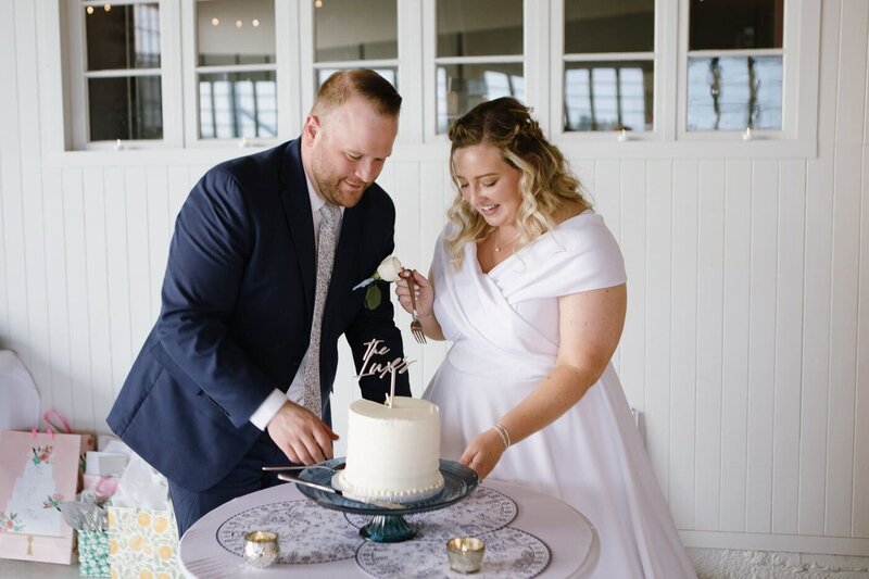 Smiling bride and groom cut their wedding cake together. 