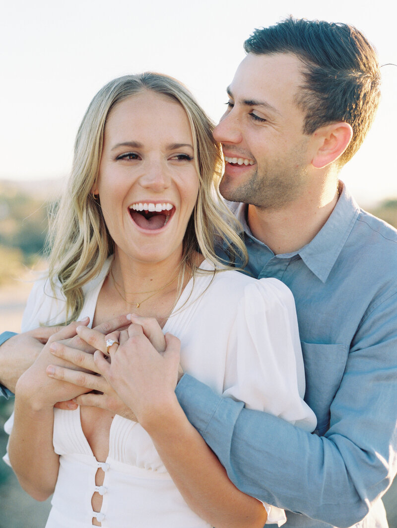 couple laughing holding eachother with white reformation dress and blue button down