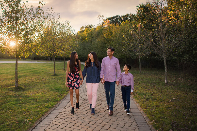 A family of 4 with coordinated outfits holding hands and walking down a path at a park.