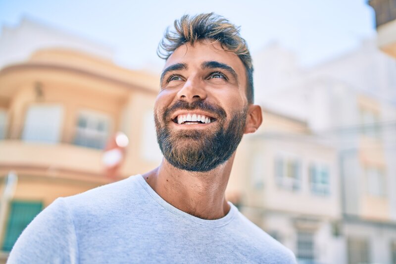 Close-up of attractive young hispanic man with beard smiling while walking through the city