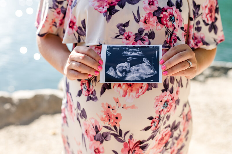 Pregnant woman holding ultrasound photo in front of stomach