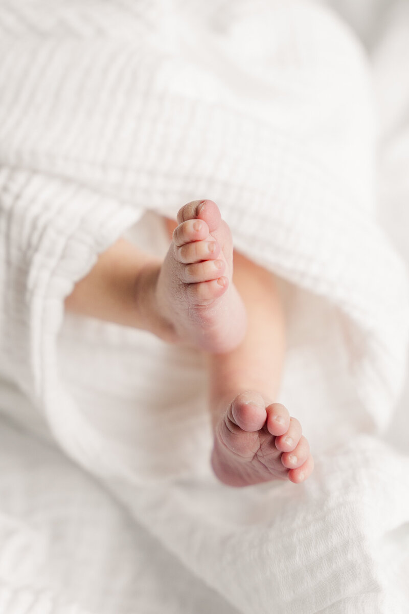 Close-up of a newborn's feet wrapped in a soft, neutral-toned blanket, highlighting their small size