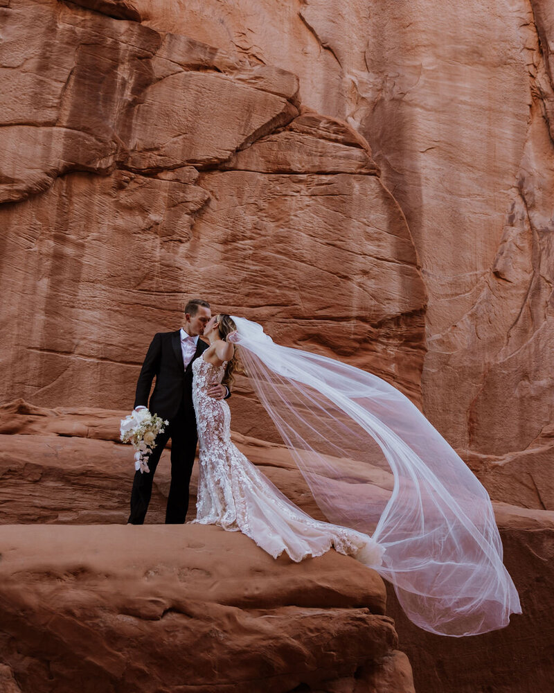 bride and groom kissing in arches National park with the veil blowing in the wind