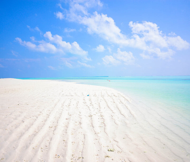 White sand beach with aqua water and a light blue sky with wispy clouds.