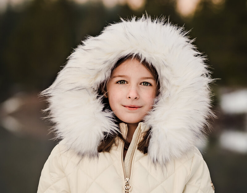 Portrait of a young girl in a winter fur jacket and hood, against a winter mountain backdrop