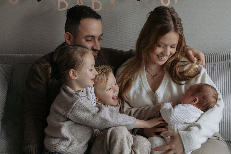 Een gezin zit op een bank met een baby, genietend van samen tijd doorbrengen in een gezellige woonkamer.