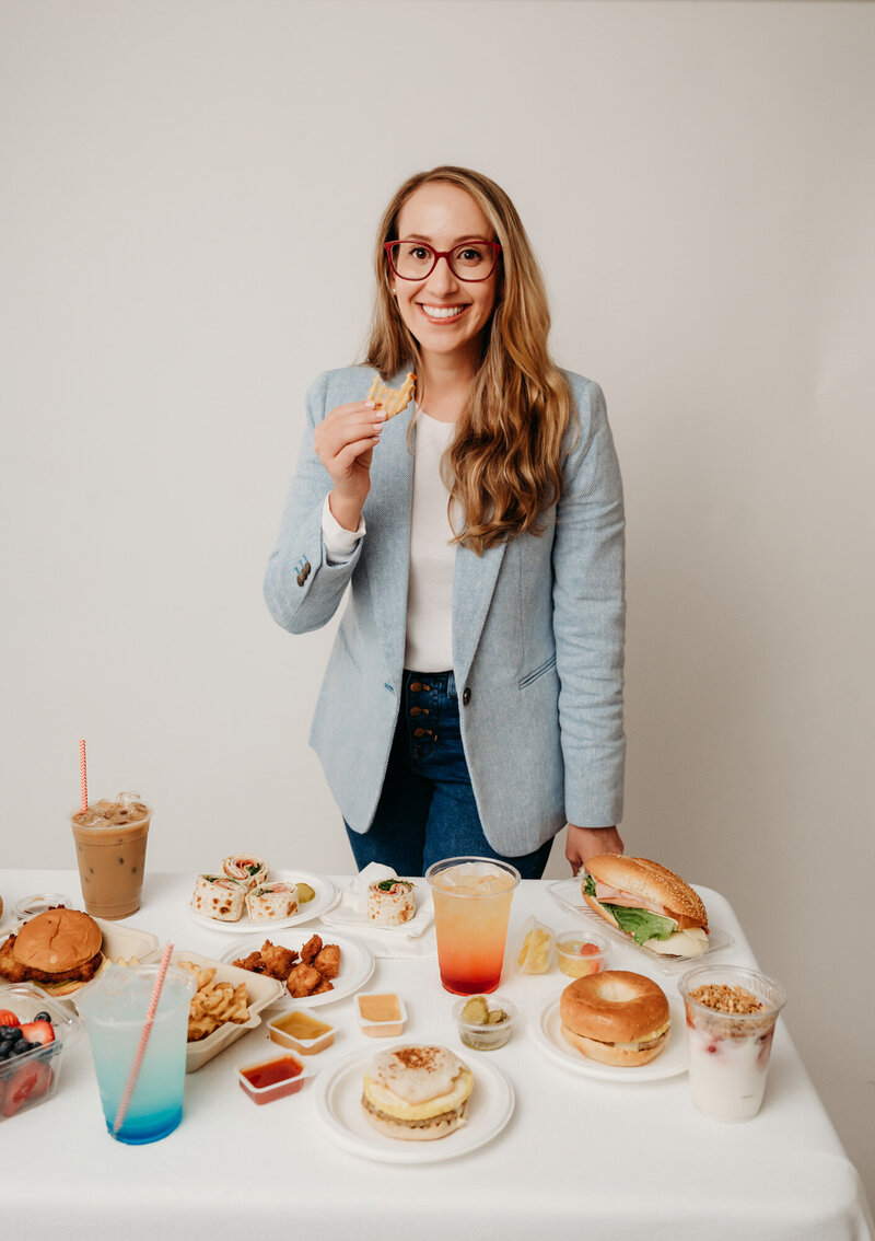 Rachel Toner, food sensory scientist and owner of Taste Strategy, holding a waffle fry and standing next to table of food