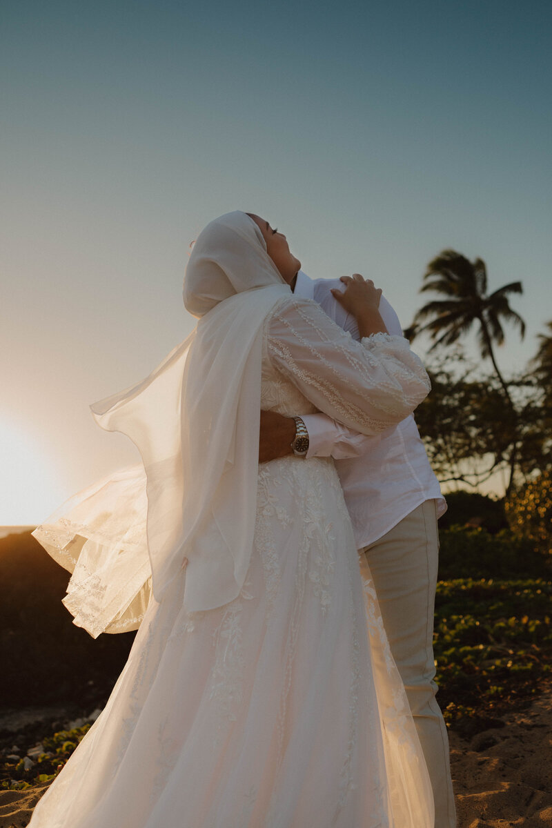 bridge and groom hugging on beach in hawaii