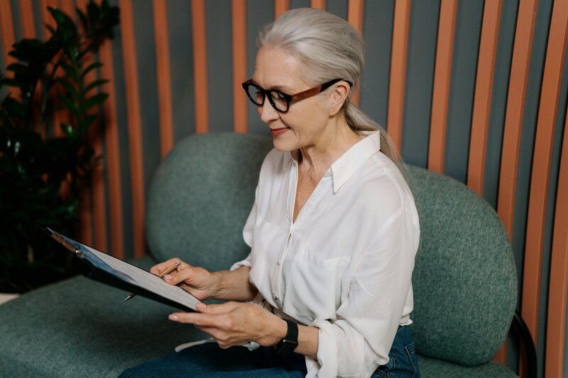 middle aged woman with silver hair sitting on sofa with clipboard
