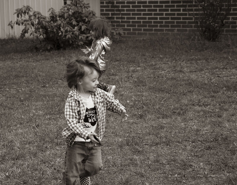 A toddler runs around his yard with his cousin during a lifestyle photoshoot.