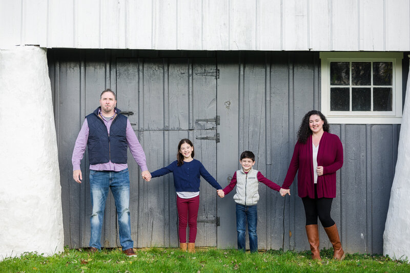 A family of four holding hands and walking together during a mini session at Valley Forge, surrounded by vibrant autumn scenery