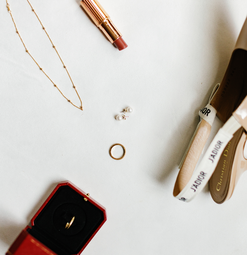 Flat lay of bridal accessories including a gold ring, pearl earrings, a necklace, lipstick, and Dior shoes, captured by Claudia Amalia, a wedding and lifestyle photographer based in Miami, Florida.