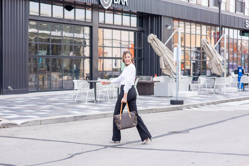 Stylish woman walking across the street swinging her bag as a prop