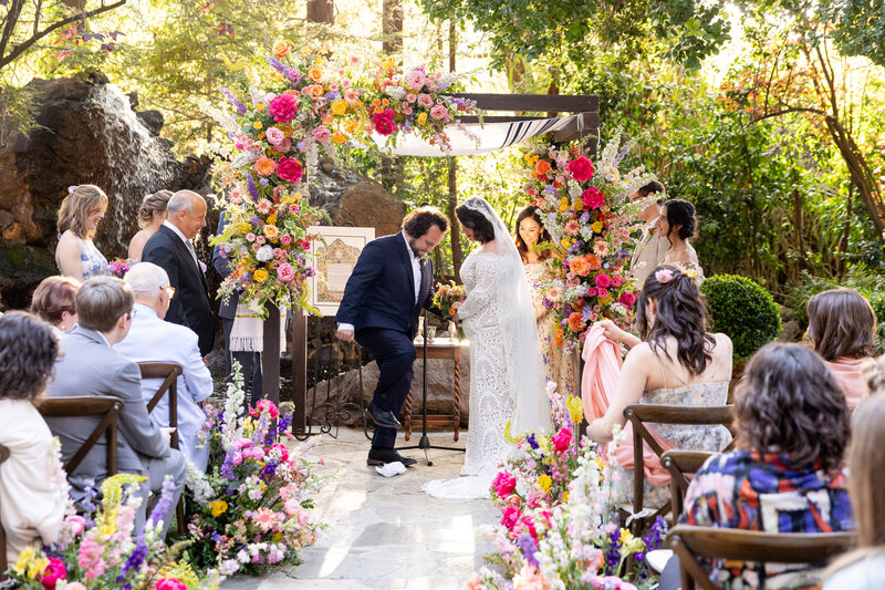 A groom stepping on a piece of glass during their wedding ceremony