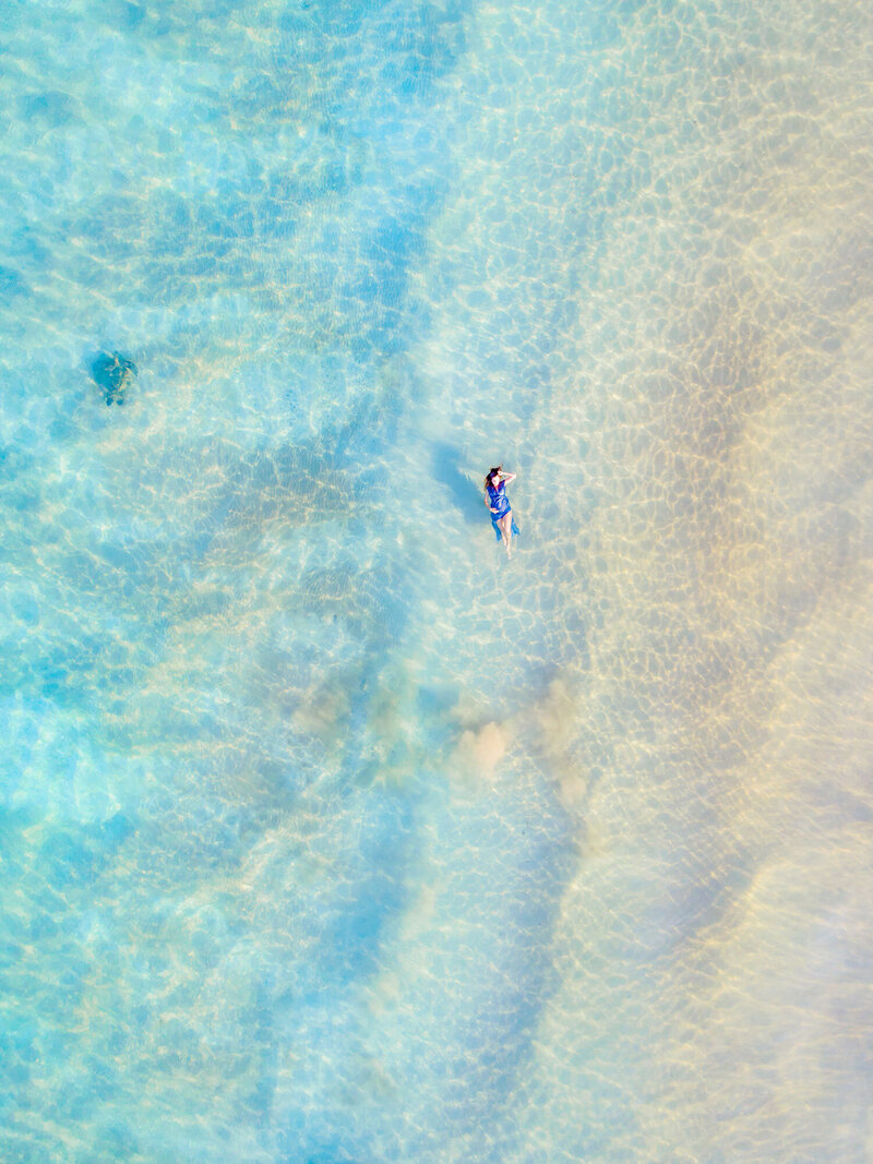 Drone portrait of pregnant woman floating on her back in the ocean during a Love + Water photoshoot