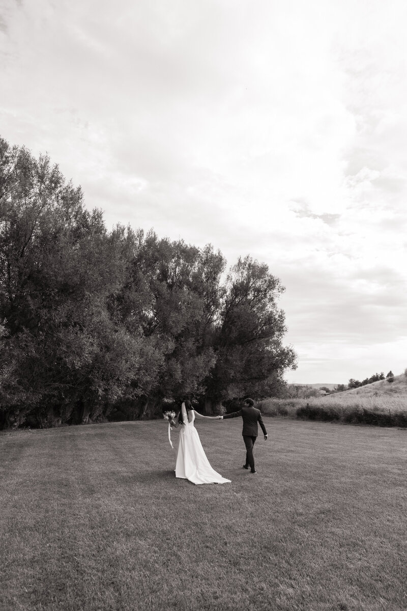 Bride and groom walking hand in hand away from camera at Bissel Creek Meadows in Emmett, Idaho