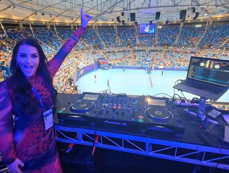 DJ in red shirt standing beside a full deck setup at the Brisbane International tennis tournament