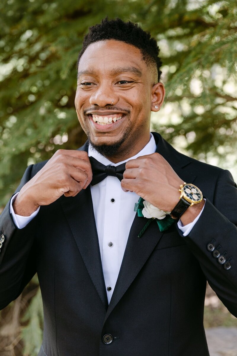 portrait of a groom adjusting his bow tie outdoors in Aspen, Colorado