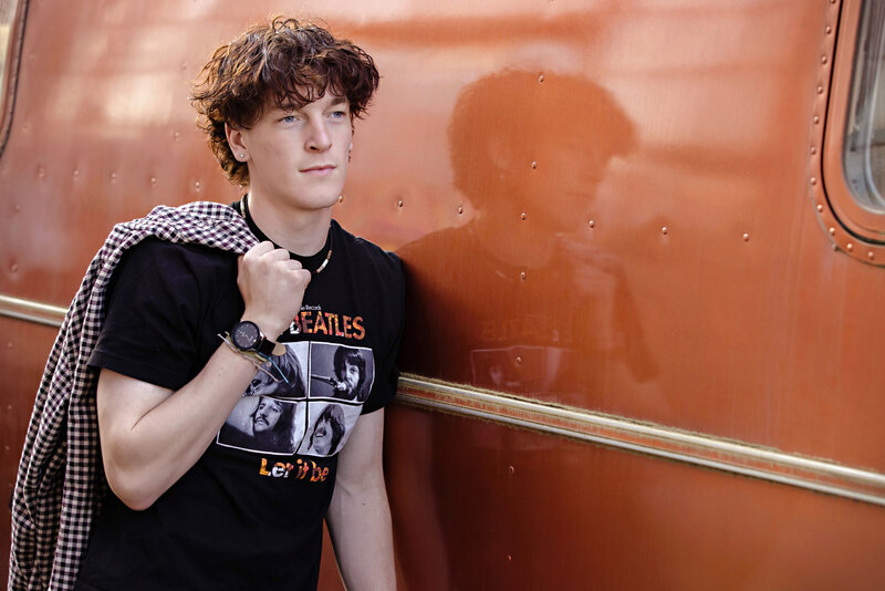 Male HS Senior in a black Beatles concert t-shirt with a checkered jacket over his shoulder leaning against an orange metallic van showing his reflection.
