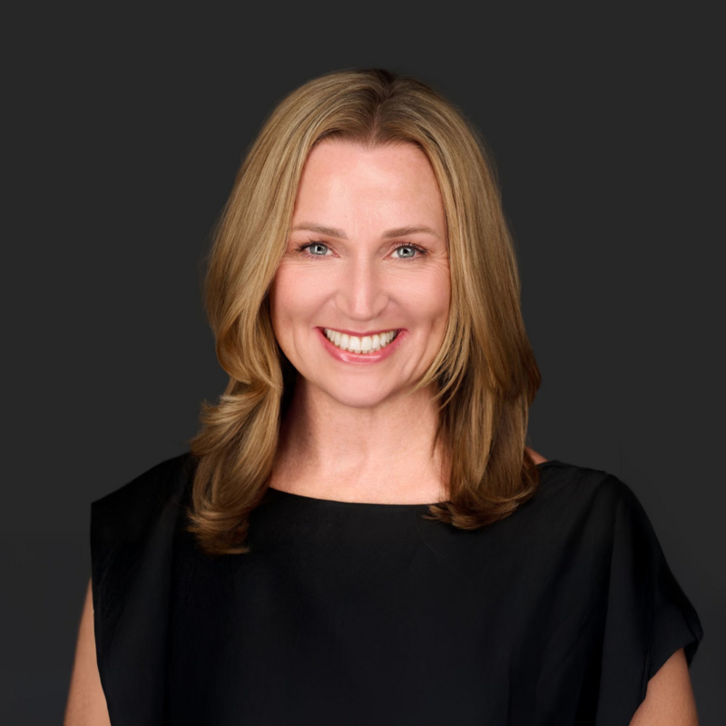 Jenn Cloutier, self-leadership coach, smiling warmly with shoulder-length blonde hair, wearing a black professional top against a dark gray background.