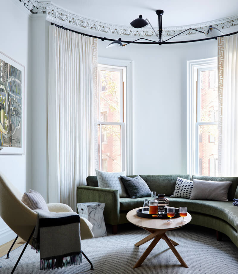 A modern living room in a Boston brownstone by interior decorators in Boston MA, featuring original historic details, a custom curved sofa, and mid-century modern furniture.