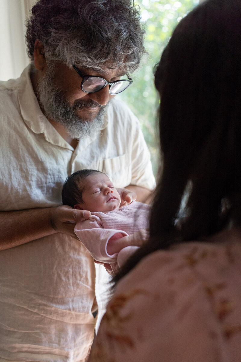 A father holds and looks down at his newborn in his home.