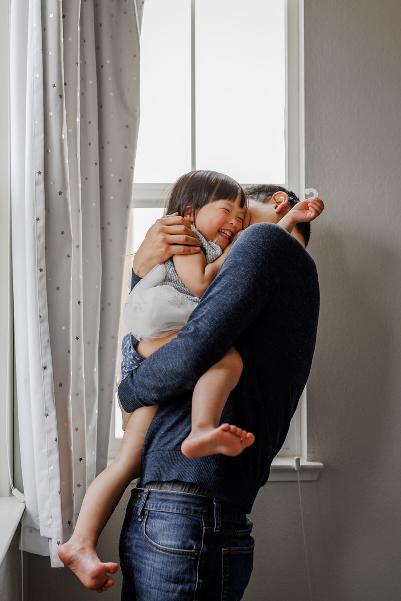 dad holding daughter in front of window making her laugh