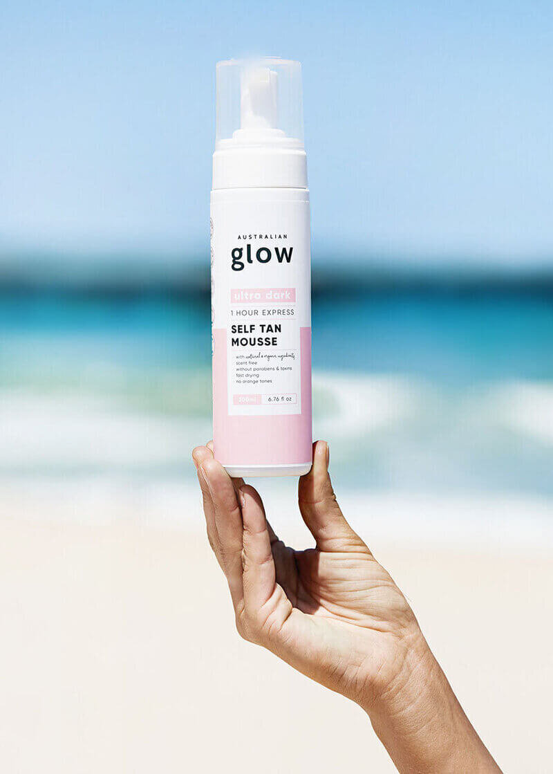 Woman holding Australian Glow tanning product on beach.