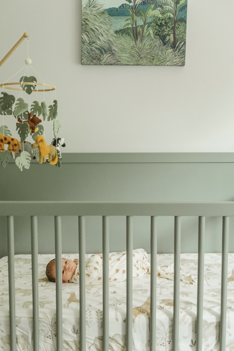 Soft green nursery with baby looking through crib rails – newborn photographer Lancaster, PA