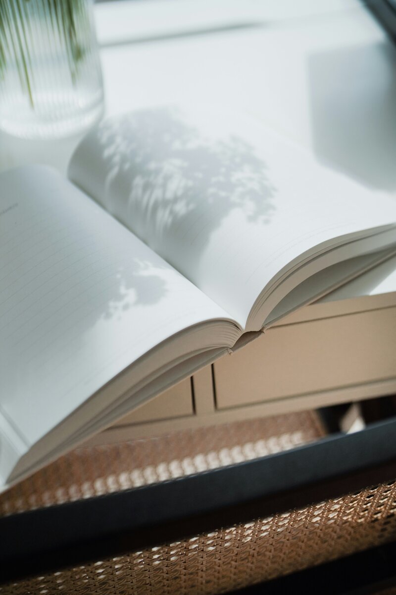 Open blank journal sits atop a desk with shadows of flowers on it