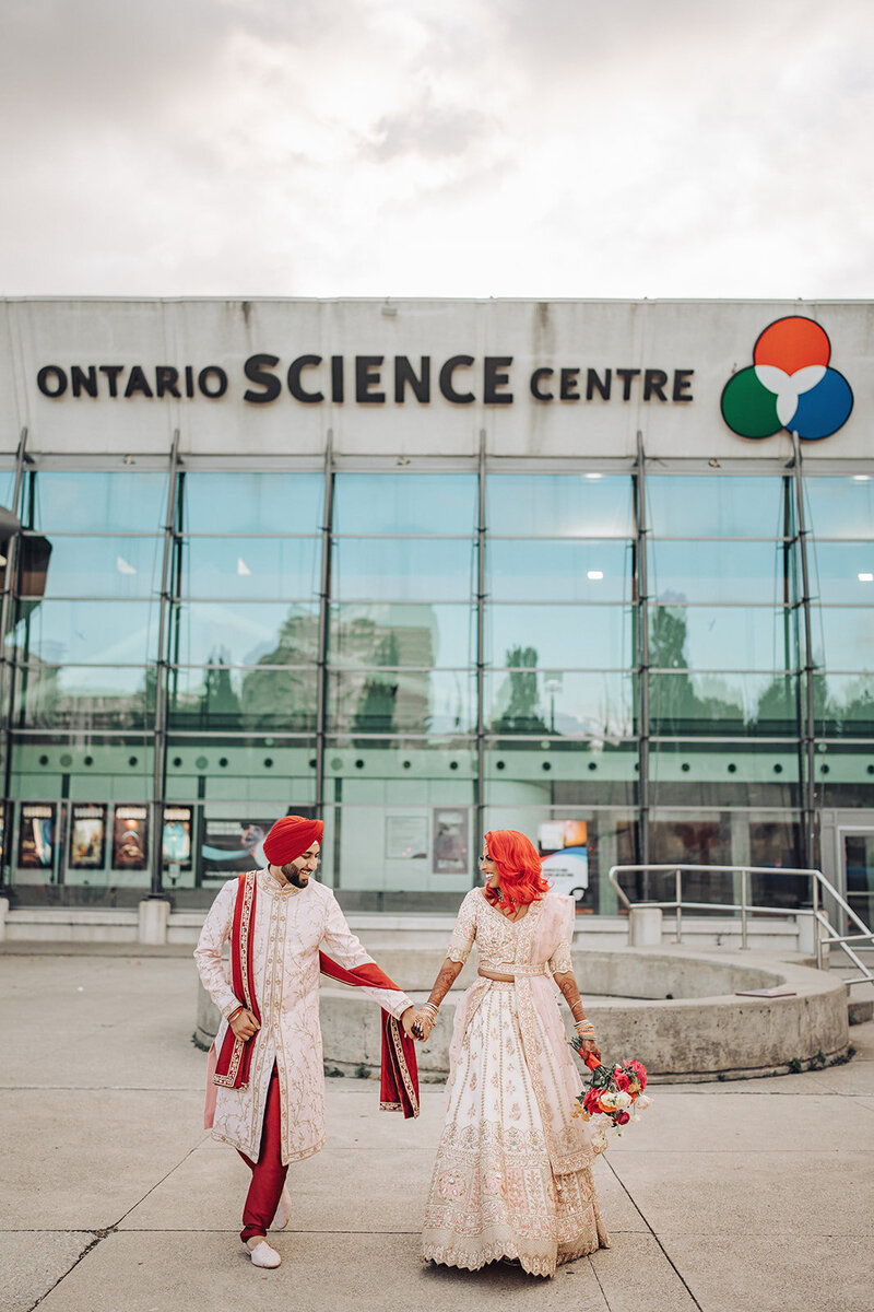 bride and groom holding hands in front of Ontario Science Centre