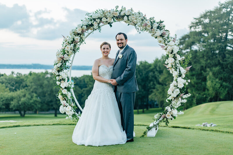 Bride and groom pose for a portrait underneath floral arch