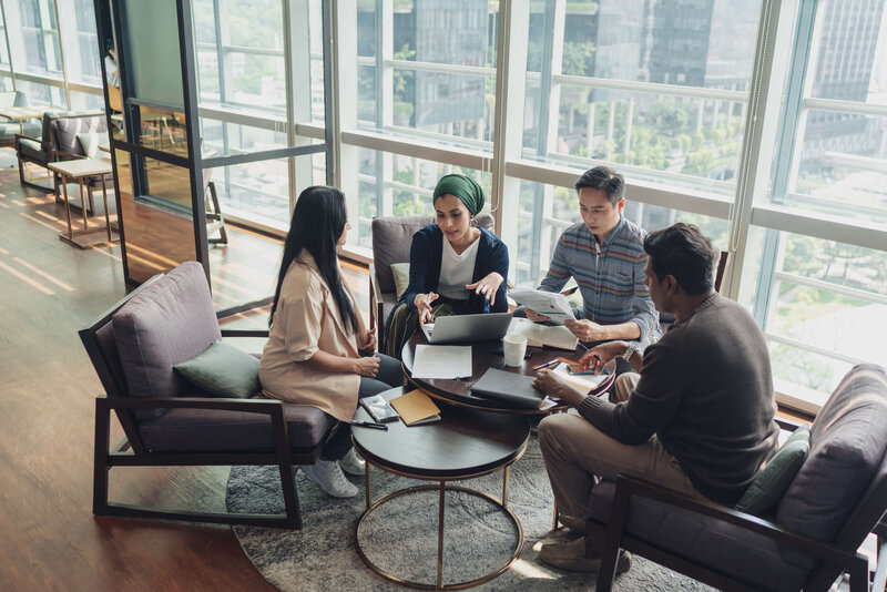 Team of four professionals collaborating on documents in a modern office lounge.