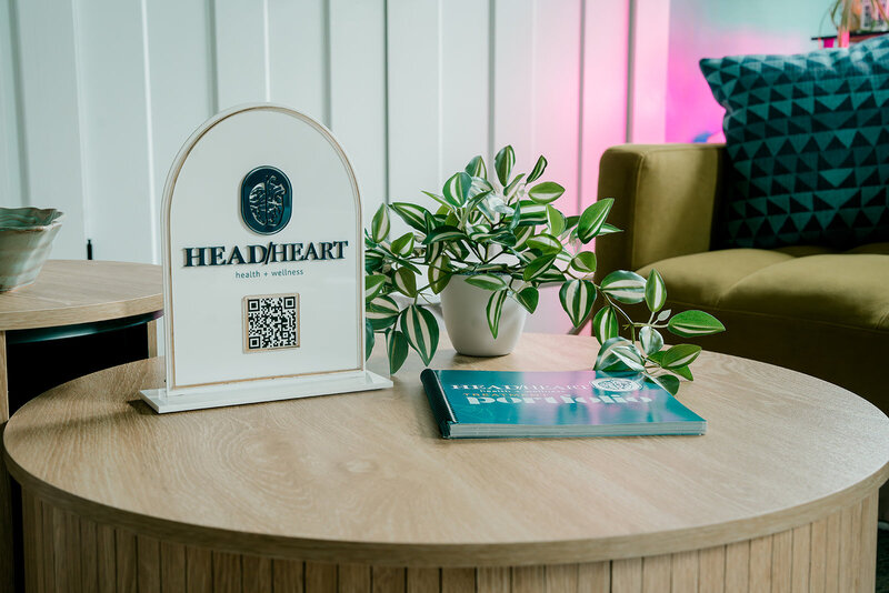 A sign for Head + Heart Health and Wellness sits on a table with a plant