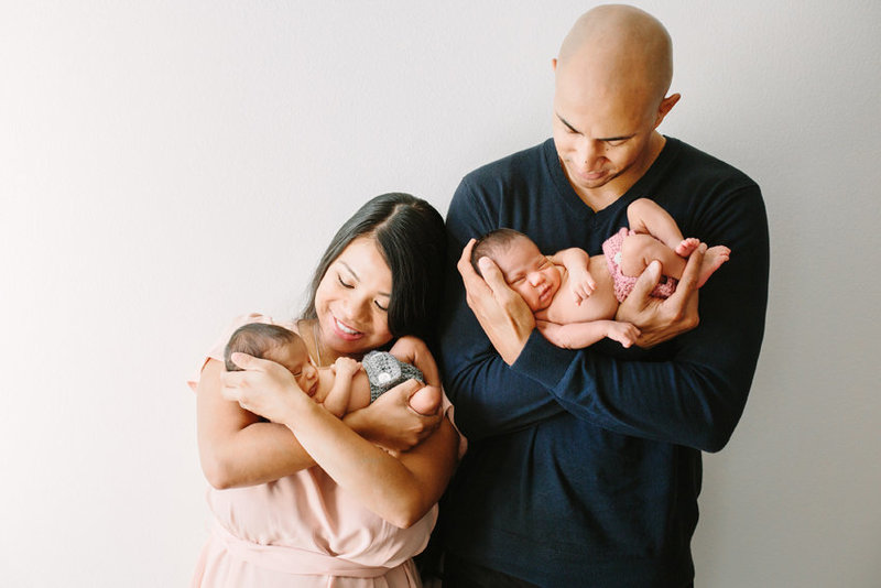 Parents each hold one of their newborn twins during their newborn portrait session
