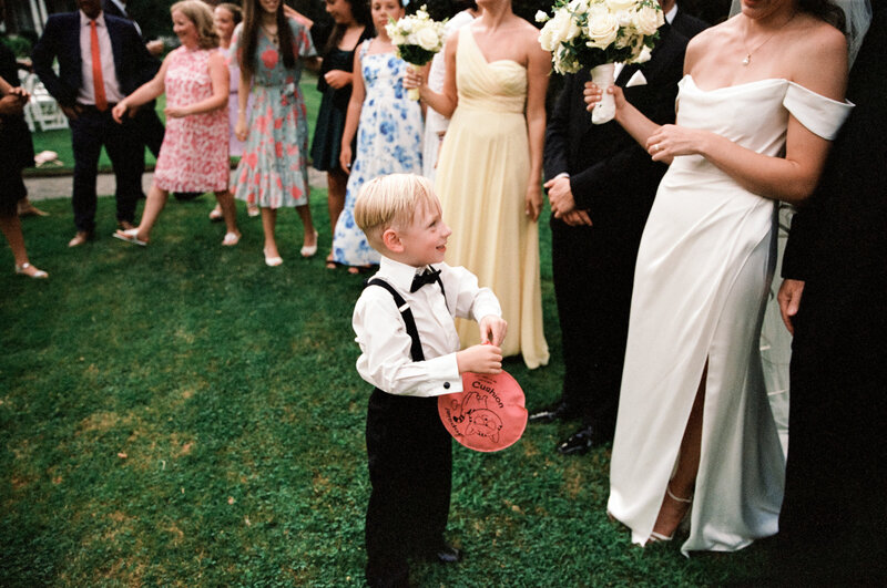 Film photo of a young ring bearer holding a balloon and smiling at the bride during a joyful group moment at a wedding at the Garden at Elm Bank in Massachusetts — captured by a film wedding photographer.
