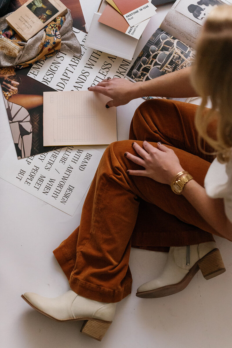 Woman in orange pants sorting through paper and pictures on the floor