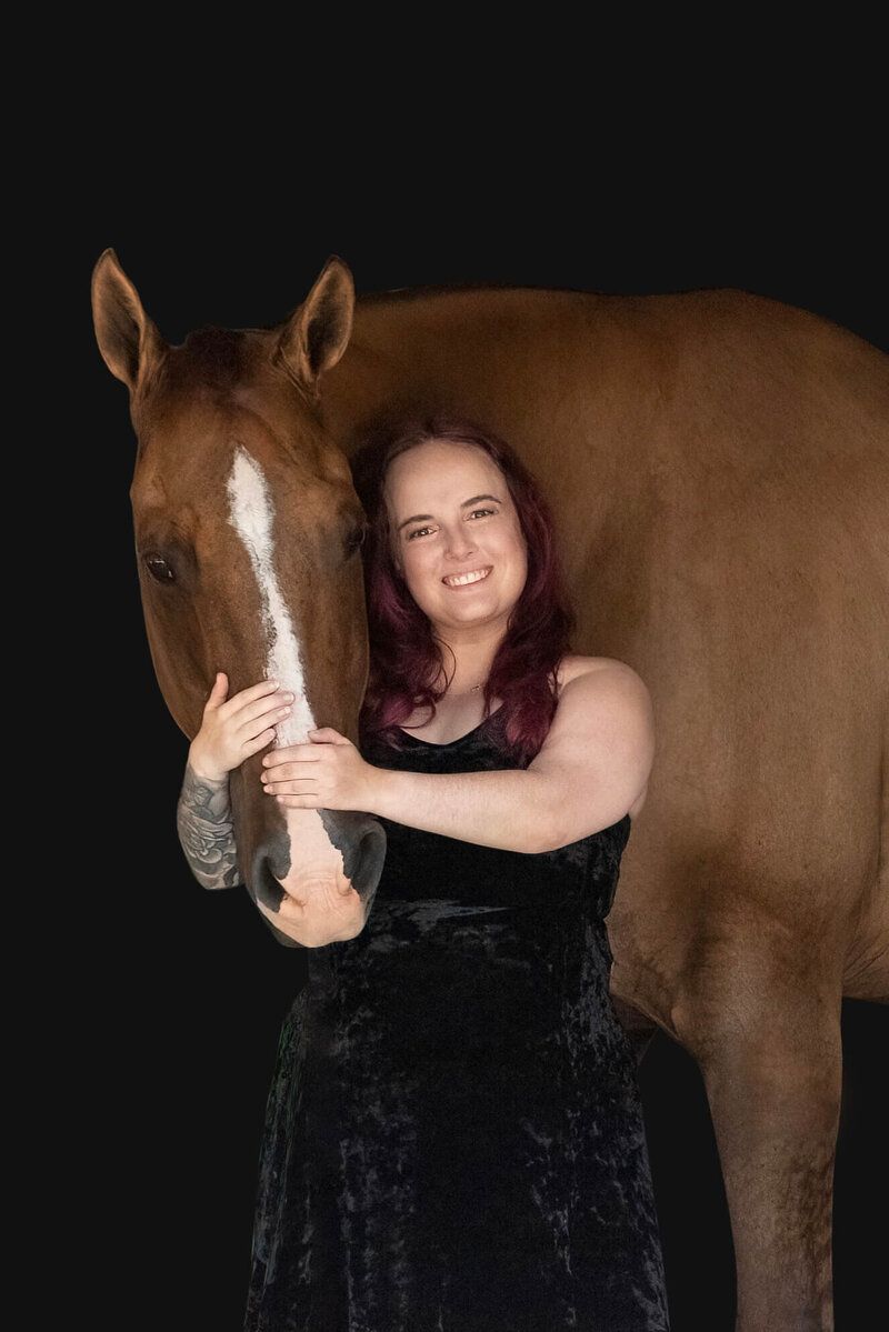 equine and pet photographer, katy in design, pictured smiling next to chestnut horse on a black background