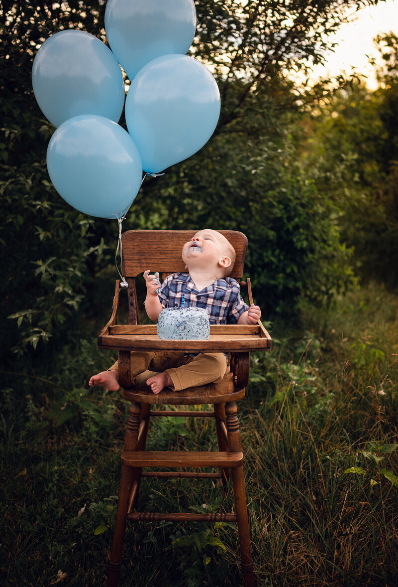 baby boy eating birthday cake in high chair with balloons